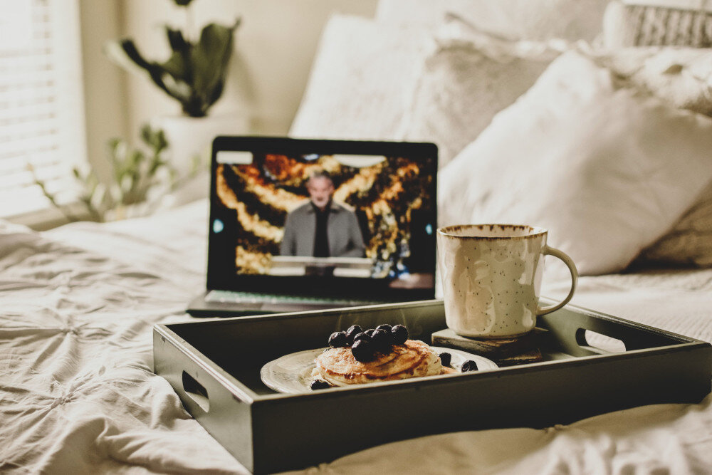 Abgebildet ist ein Tablett mit Pancakes, die mit Blaubeeren dekoriert sind und einem Kaffee. Es gibt Frühstück im Bett, begleitet von einem Video, das auf einem Tablet abgespielt wird.  | © pexels-sarah-kreusel-4165284