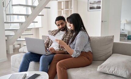 junges Paar vorm Laptop mit Papieren und Rechnungen